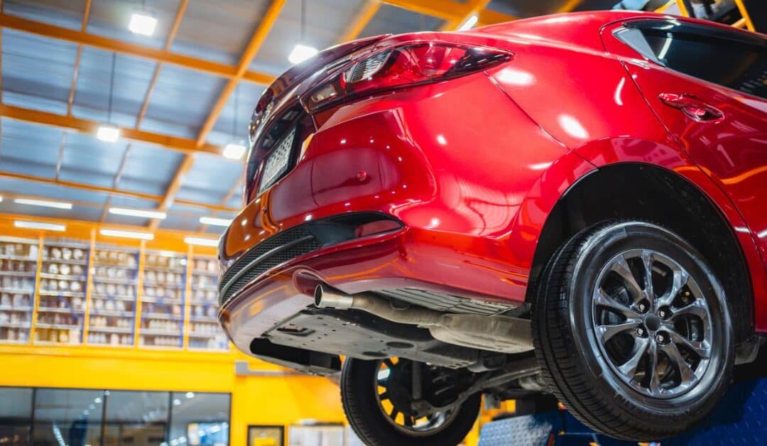Red car on a lift receiving aluminum auto body repair at West Delray Collision near Delray Beach