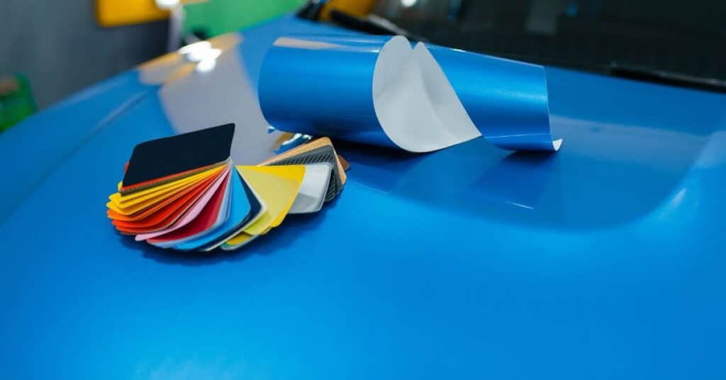 Auto Paint Color Matching Samples - West Delray Collision Center Color sample cards and a blue vinyl sheet placed on a car hood during an auto paint matching process.