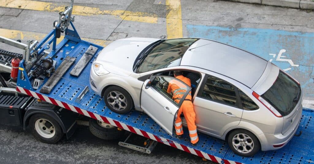 Wheel-lift tow truck securing a damaged car for transport after an accident.